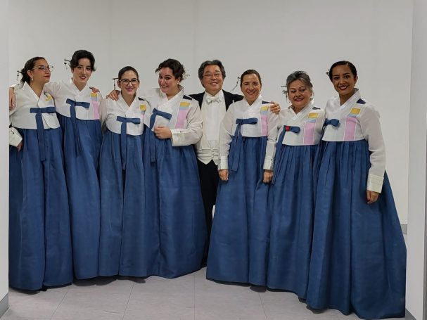 Grupo de ocho personas vestidas con hanbok tradicional en un entorno interior.