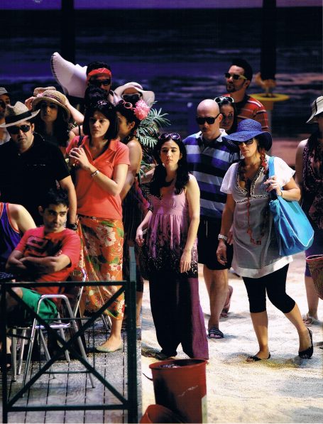 Grupo de personas caminando por la playa, algunas llevan ropa de verano y sombreros.