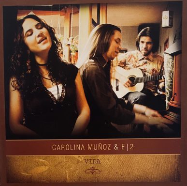 Carolina Muñoz y dos músicos, uno con guitarra y otro al piano, en un ambiente musical.