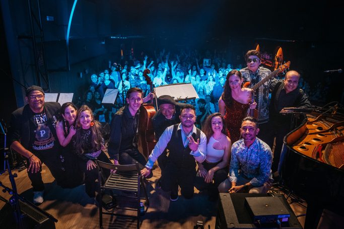 Grupo musical posando frente a un público emocionado en un concierto.